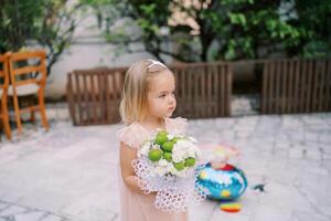 peu fille avec une bouquet de fleurs des stands dans le Cour de le maison et regards une façon photo