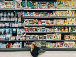 boudva, Monténégro - 01 décembre 2023. peu fille choisit une ensemble de jouets séance sur le sol dans une supermarché photo