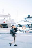 mère avec une peu fille dans sa bras des promenades le long de le promenade passé amarré yachts. côté vue photo