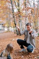 peu fille squats suivant à sa papa qui est lancement sec feuilles en haut. retour vue photo