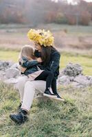 mère dans une couronne de Jaune feuilles chatouille une peu fille séance sur sa tour sur le pelouse photo