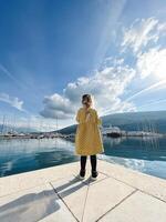 peu fille des stands sur le jetée et regards à le Marina avec yachts sur le Contexte de le montagnes. retour vue photo