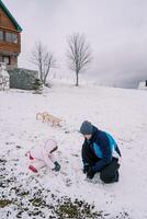 papa et une peu fille sont squat sur une colline près une traîneau et fabrication boules de neige photo