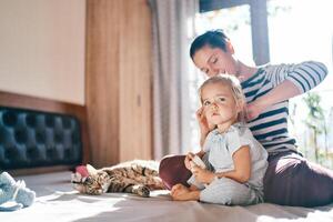 maman peignes une peu fille séance derrière sa sur le lit près une mensonge chat photo