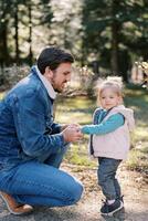 peu souriant fille des stands suivant à squat papa en portant le sien mains dans le parc photo