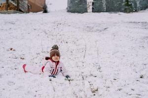 peu fille mensonges sur sa estomac dans une neigeux clairière, penché sur sa mains photo