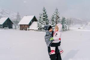 maman regards à une peu fille dans sa bras tandis que permanent dans une neigeux village dans une Montagne vallée photo