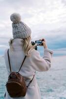 fille des stands sur le rivage et photographies le horizon avec une téléphone intelligent. côté vue photo