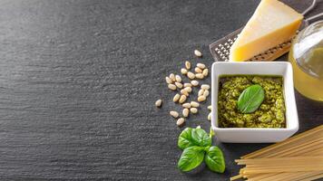 fait maison Pesto sauce dans petit carré pot et Ingrédients pour Pâtes sur noir ardoise Contexte photo