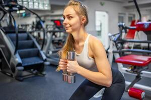 Jeune femme détient haltères dans sa mains et travaux en dehors dans le Gym performant un exercer. haute qualité photo