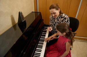 magnifique peu pianiste fille pièces piano, composition une mélodie en dessous de le orientation de sa prof pendant individuel la musique leçon à maison. les enfants. éducation. modes de vie. loisirs et divertissement photo