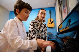 femelle pianiste, la musique prof enseignement piano et la musique leçon à une adolescent garçon dans blanc décontractée chemise, séance ensemble à en bois piano. personnes. mode de vie. éducation. loisirs et loisir photo