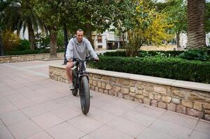 plein longueur portrait de une Beau caucasien homme location électrique vélo, équitation dans le ville. bicyclette partage ville un service photo