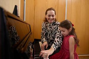 de bonne humeur magnifique femme pianiste, musicien prof souriant tandis que performant mélodie sur piano, expliquant la musique leçon à sa étudiant fille photo