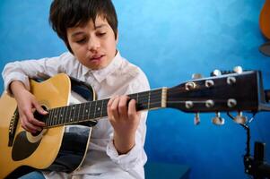 adolescent garçon pianiste cueillette le cordes tandis que en jouant le acoustique guitare. sur de soi adolescente garçon apprentissage à jouer guitare pendant une la musique leçon. photo