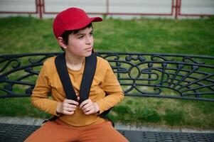 sac à dos milieu est adolescent, écolier à la recherche de côté, séance sur une banc dans le parc après école photo