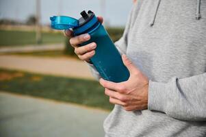 sélectif concentrer sur le l'eau bouteille dans le mains de un actif Masculin athlète repos après faire des exercices ou fonctionnement Extérieur photo