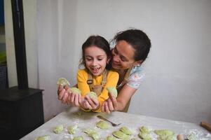 maman et fille avoir amusement tandis que cuisine Dumplings, permanent ensemble à fariné cuisine table photo