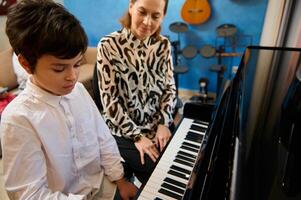 Beau adolescent garçon prise piano leçon, passionnément en jouant le clés en dessous de sa enseignants conseils, sentiment le rythme de musique. musical éducation et Talent développement dans le progrès photo