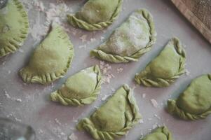 fermer Dumplings de vert Couleur sur une fariné table Contexte. traditionnel cuisine dans Ukraine - varennyky avec en purée patates et épinard photo