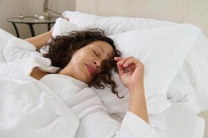 détendu Jeune femme en train de dormir dans sa lit couvert avec blanc doux couverture. femme sieste dans le Matin. ses temps à nous en haut photo