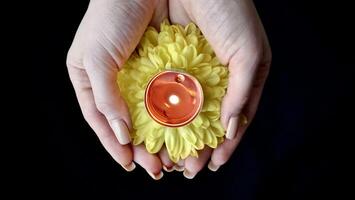 fête de le religieux Indien Festival de Diwali. Jaune fleurs dans femme main avec brûlant Holi bougies à hindi Festival fermer, isolé, noir Contexte photo