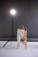 une Écossais tout droit oreille chat dans costume et une rouge attacher est assis sur une chaise dans une noir et blanc vidéo production studio, verticale photo
