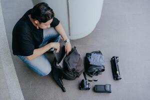 indonésien Masculin photographe est emballage bagage et avoir prêt à Voyage. vacances Voyage concept. photo