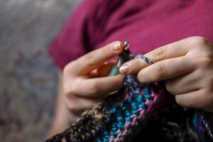 Jeune femme mains crochet coloré la laine veste avec fil séance dans le confortable fauteuil à maison. femelles les doigts en portant métal crochet crochets. sélectif se concentrer. photo