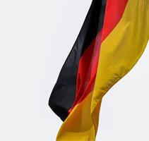 drapeau de Allemagne agitant dans le vent sur le en bois mât de drapeau. allemand nationale drapeau fabriqué de soyeux tissu, noir, rouge, Jaune. isolé sur le blanc Contexte. coupure chemin. copie espace. photo