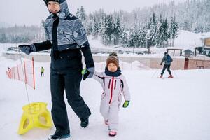 maman avec une traîneau et une peu fille montée en haut le flanc de coteau en portant mains photo