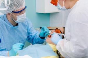 une Masculin dentiste avec dentaire outils exercices le les dents de une patient avec un assistant. le concept de médecine, dentisterie et soins de santé photo