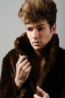 séduisant jeune homme portant un manteau de fourrure avec une coiffure moderne photo