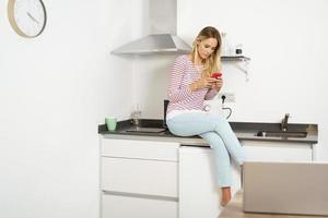 penser belle femme utilisant son smartphone assis dans la cuisine à la maison photo