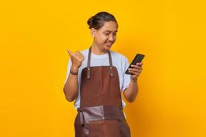 Portrait d'un bel homme gai regardant un téléphone portable avec un doigt montrant une remise sur les ventes sur fond jaune photo