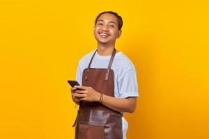 portrait de joyeux barista beau regardant vers l'avenir et tenant un smartphone sur fond jaune photo