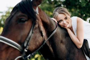 fille dans une robe d'été blanche sur une promenade avec des chevaux bruns photo