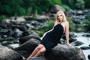 fille blonde dans une robe noire aux yeux bleus sur la côte de la rivière photo