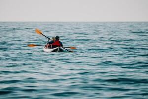 content couple kayaks dans un gonflable kayak sur le mer à le coucher du soleil. couple faire du canoë dans le mer près le île avec montagnes. gens kayak dans la vie vestes naviguer. retour vue photo