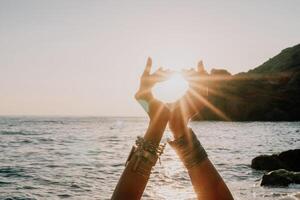 femme mer yoga. content femme dans blanc maillot de bain et boho style bracelets pratiquant en plein air sur yoga tapis par mer sur le coucher du soleil. femmes yoga aptitude routine. en bonne santé mode de vie, harmonie et méditation photo