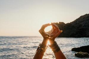 femme mer yoga. content femme dans blanc maillot de bain et boho style bracelets pratiquant en plein air sur yoga tapis par mer sur le coucher du soleil. femmes yoga aptitude routine. en bonne santé mode de vie, harmonie et méditation photo