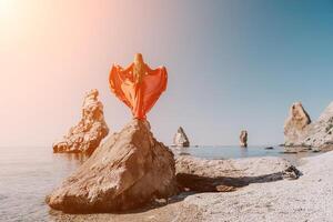 femme Voyage mer. Jeune content femme dans une longue rouge robe posant sur une plage près le mer sur Contexte de volcanique rochers, comme dans Islande, partage Voyage aventure périple photo