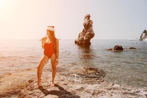 femme Voyage mer. content touristique prendre plaisir prise image sur le plage pour souvenirs. femme voyageur dans Père Noël chapeau regards à caméra sur le mer baie, partage Voyage aventure périple photo