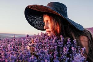 femme lavande champ. content insouciant femme dans noir robe et chapeau avec grand bord odeur une épanouissement lavande sur le coucher du soleil. parfait pour inspirant et chaud concepts dans Voyage et esprit d'aventure. proche en haut photo