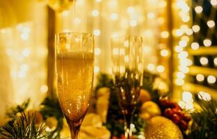 deux Champagne des lunettes rempli avec Champagne sont mis sur une table avec une fruit arrangement. le des lunettes sont entouré par lumières, création une de fête atmosphère. photo