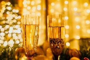 deux Champagne des lunettes rempli avec Champagne sont mis sur une table près à Noël arbre. le des lunettes sont entouré par lumières, création une de fête atmosphère. photo
