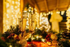 deux Champagne des lunettes rempli avec Champagne sont mis sur une table près à Noël arbre. le des lunettes sont entouré par lumières, création une de fête atmosphère. photo