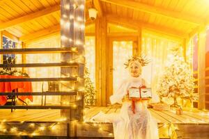 une femme dans une blanc robe en portant une cadeau boîte dans de face de une Noël arbre. photo