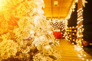 couvert de neige Noël arbre avec brillant blanc lumières situé en plein air près une bâtiment, une accueillant de fête moment. photo