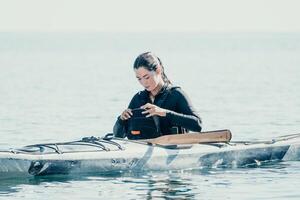 femme mer kayak. content souriant femme dans kayak sur océan, pagayer avec en bois rame. calme mer l'eau et horizon dans Contexte. actif mode de vie à mer. été vacances. photo